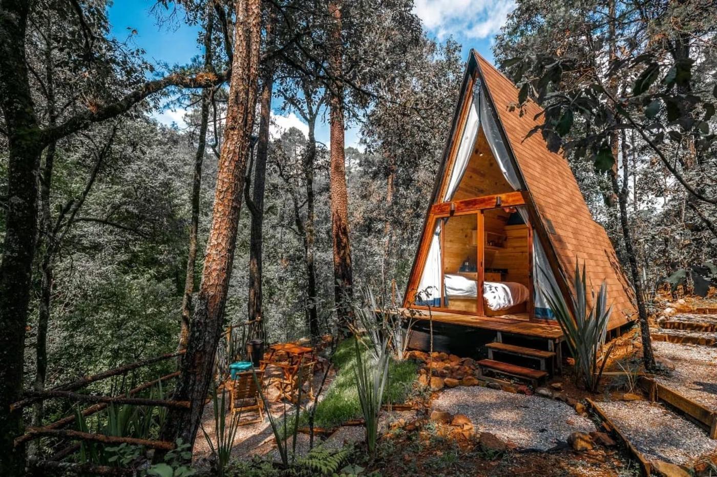Foto referencial de cabaña en A con cama y terraza entre árboles